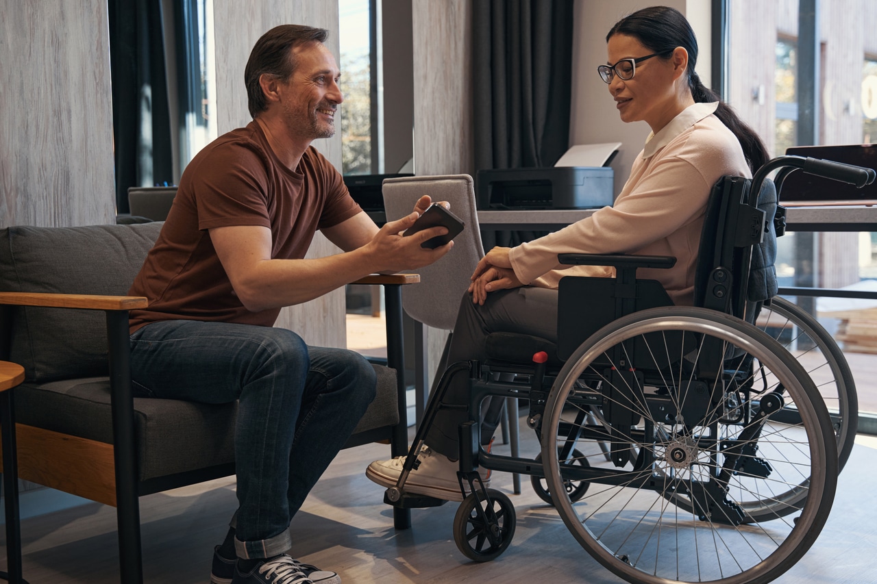 jolly man with smartphone in office with female with disability