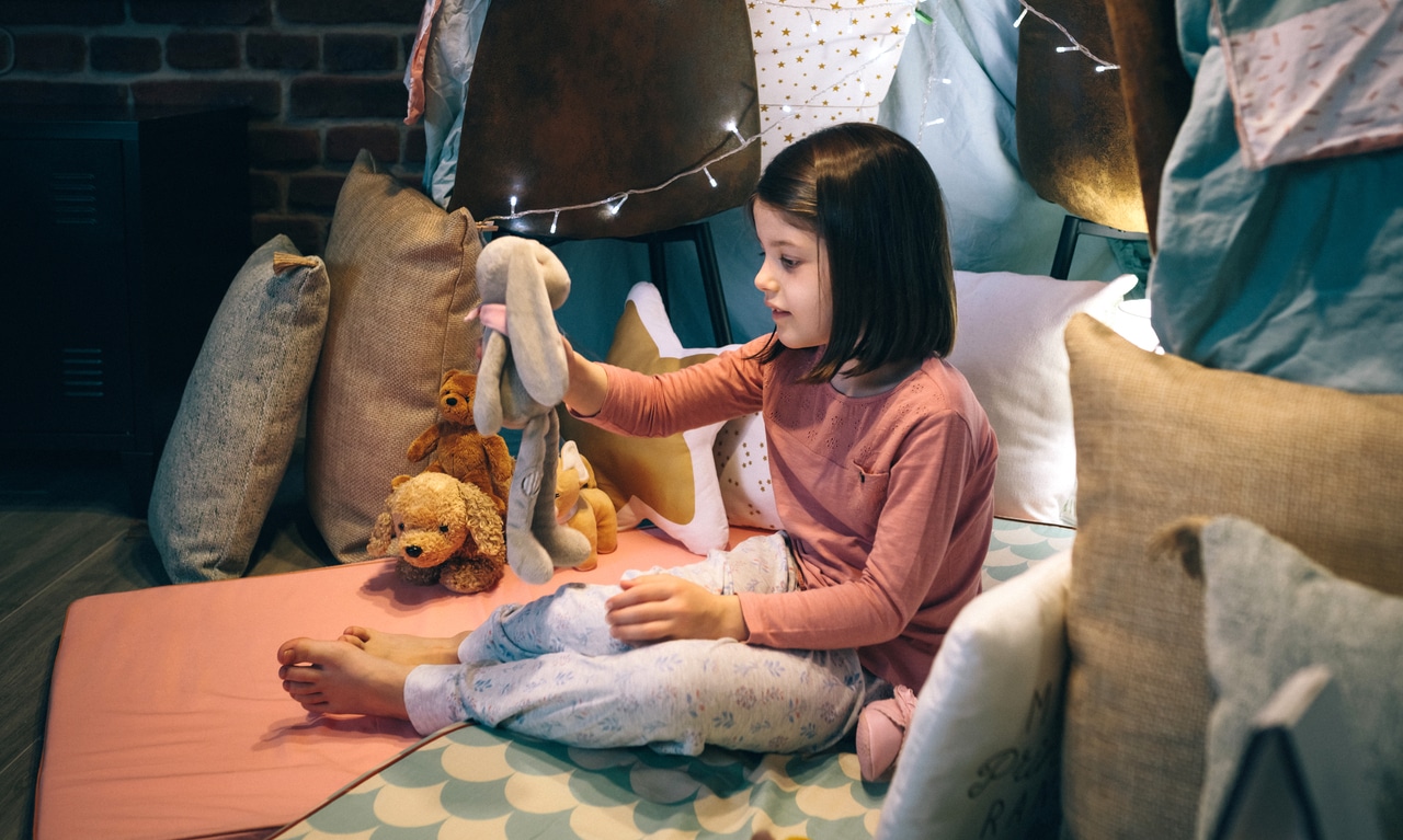 girl in pajamas playing alone with teddies in a play shelter