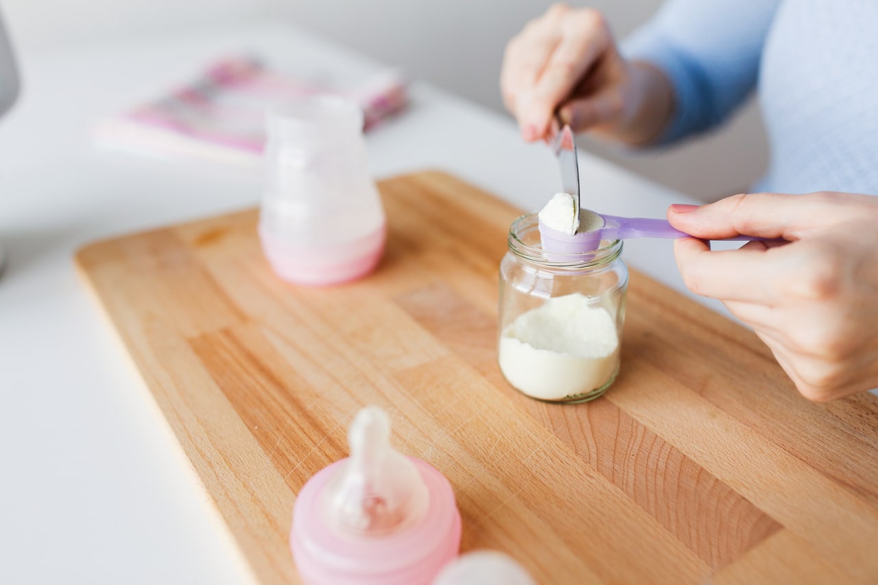 hands with jar and scoop making formula milk