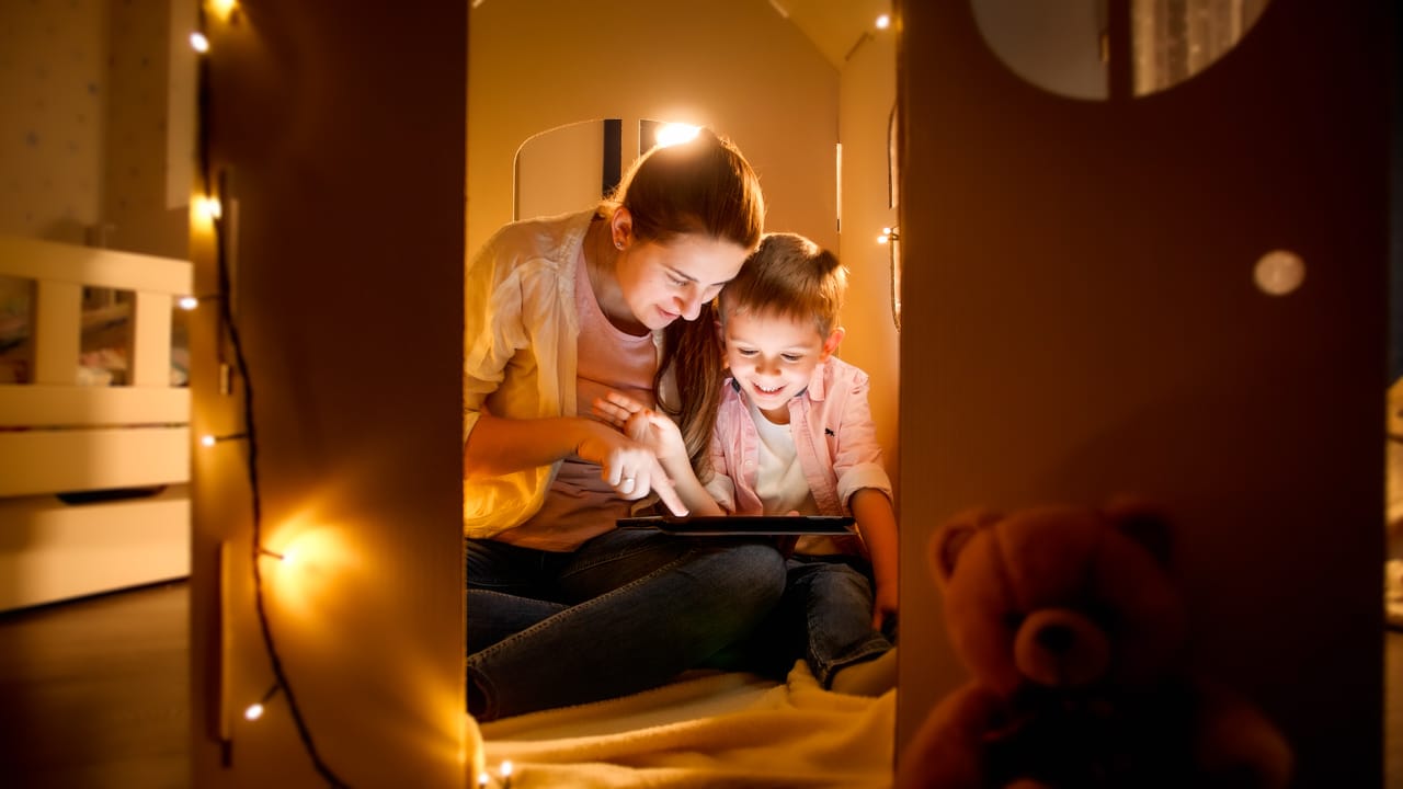 happy laughing boy with young mother playing games and using tablet computer at night before going to sleep. concept of child education and family having time together at night
