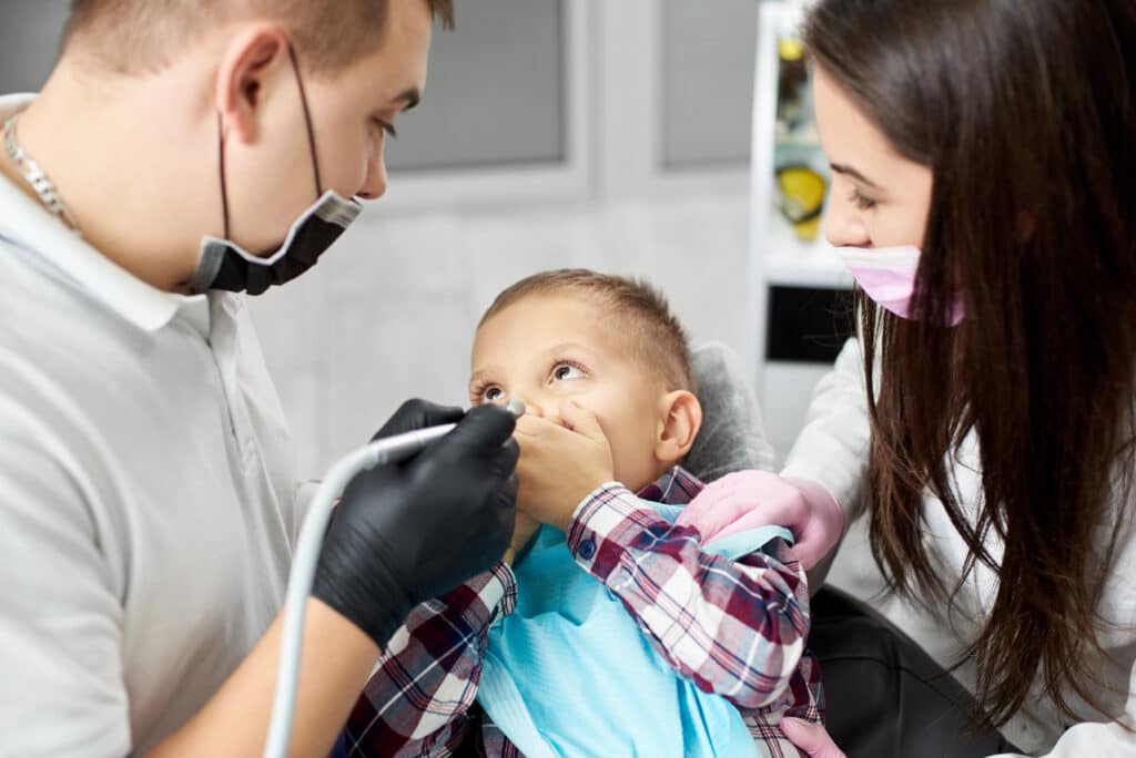 kid in a dental chair closes his mouth with his hands, fearing a dentist