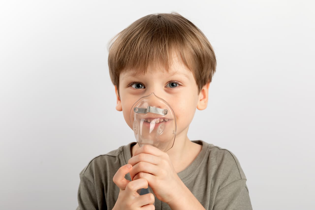 the boy breathes into the nebulizer on a light background