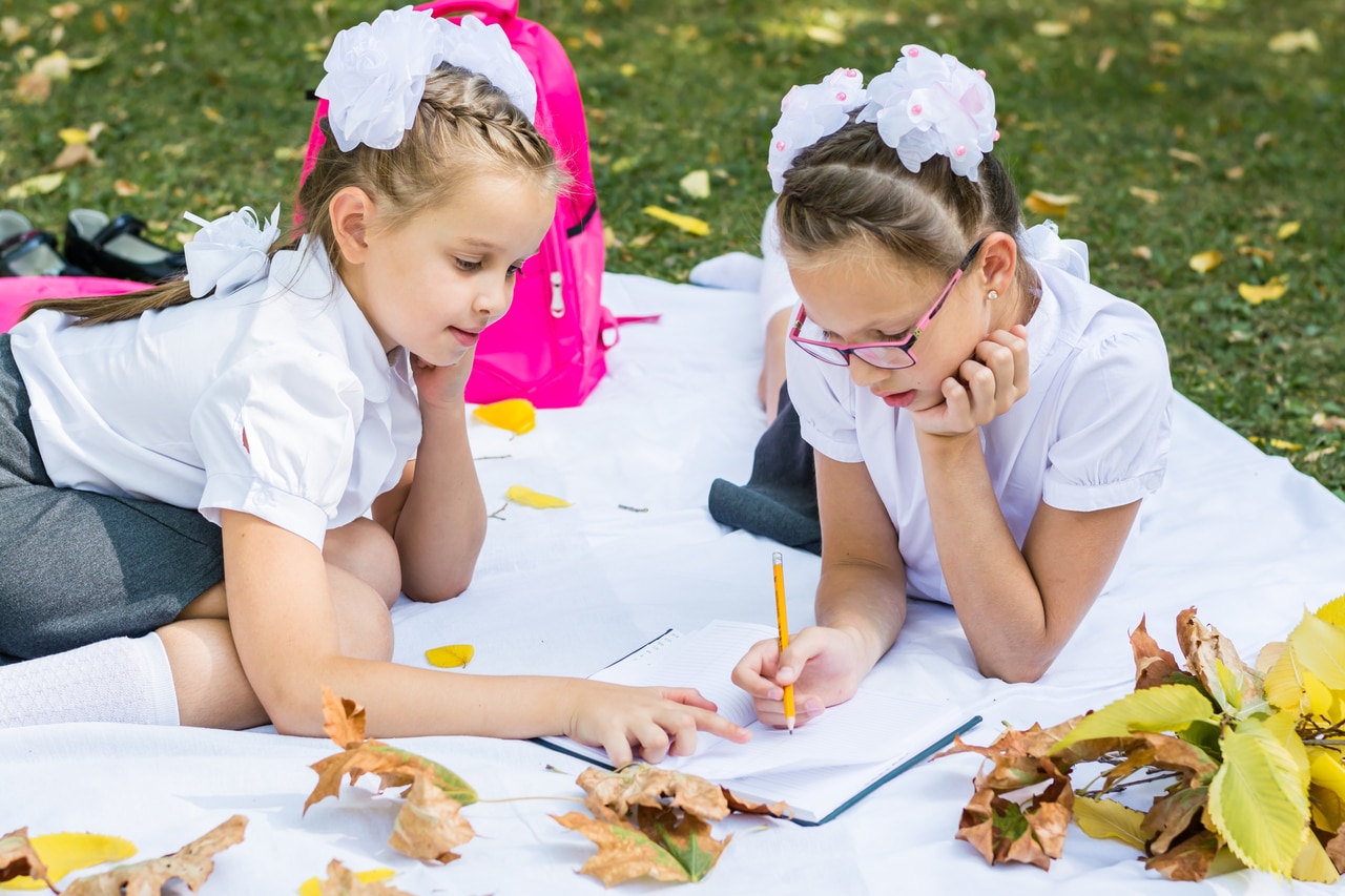 two cute schoolgirls doing homework on a blanket in a sunny autu