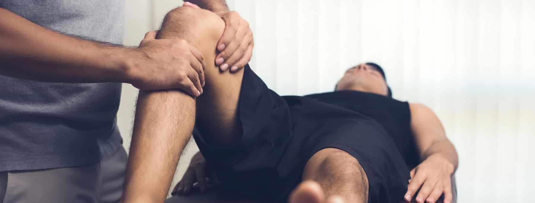 therapist treating injured knee of athlete male patient