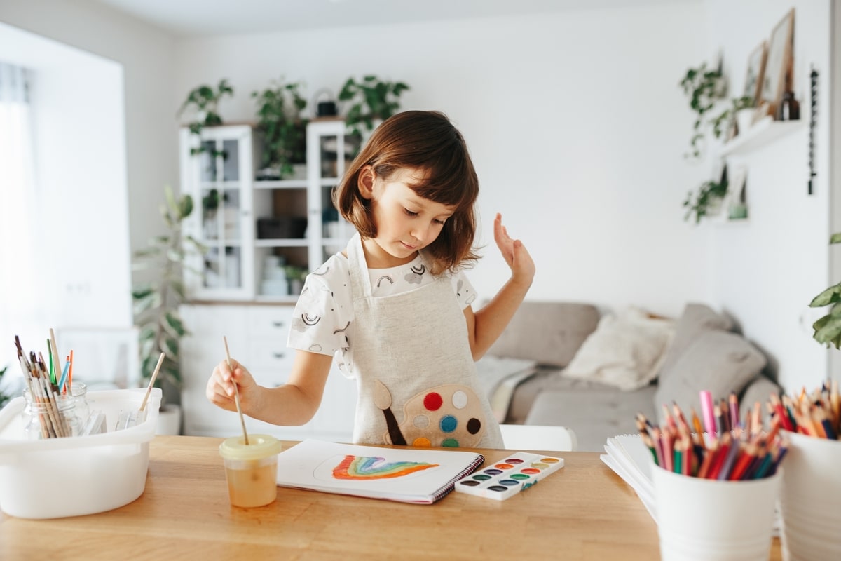 kids painting watercolor rainbows at table at home