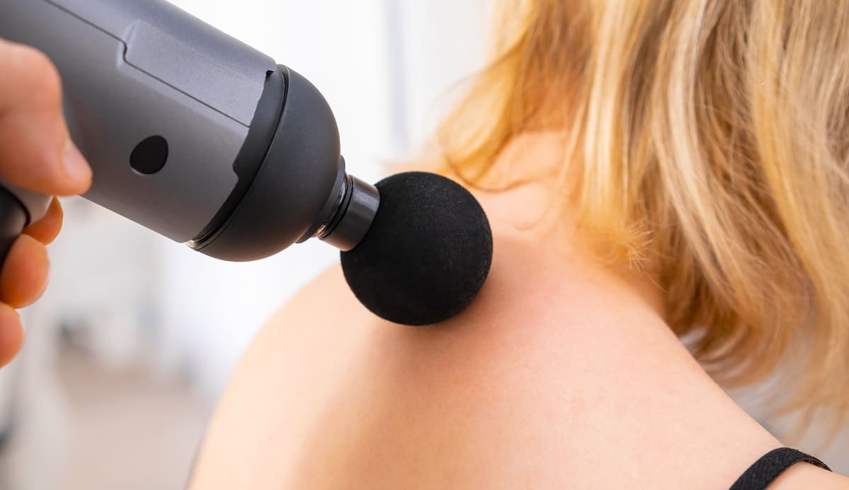 a therapist massaging a womans neck using massage gun.