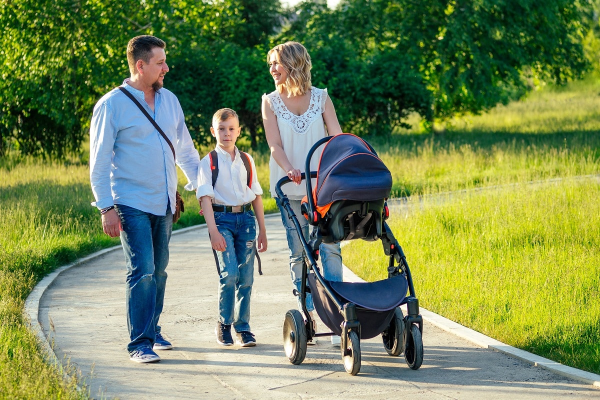 active big family father, mother, son and baby in stroller walking in the park