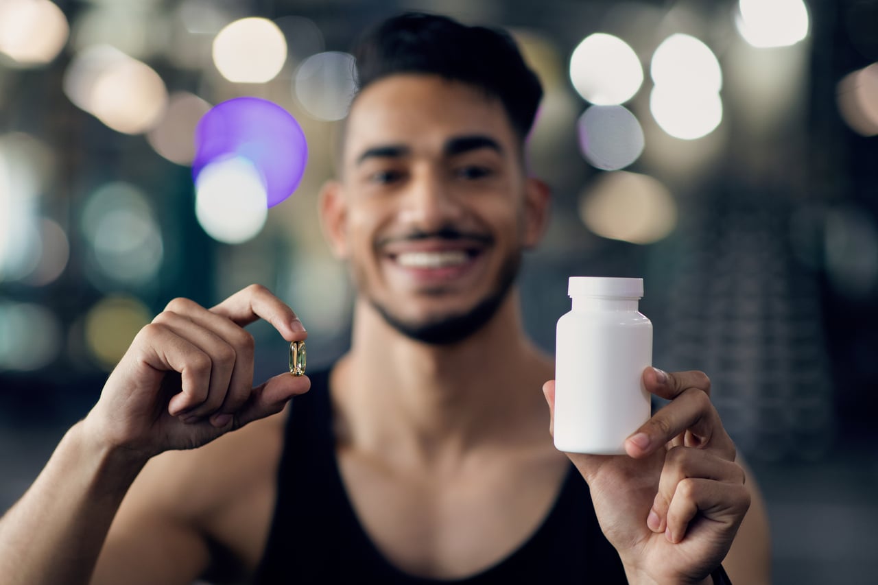 fitness supplements. sporty middle eastern guy demonstrating white jar and capsule pill