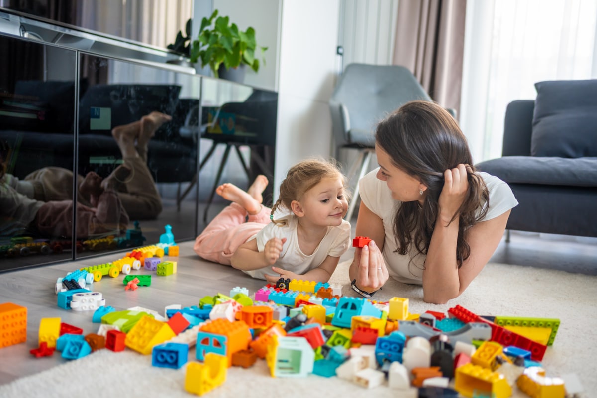 little girl play with constructor toy on floor in home with mom or woman babysitter, educational game, family at home spend leisure activities time together concept