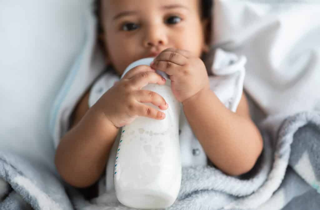 cute little african american child drinking from baby bottle