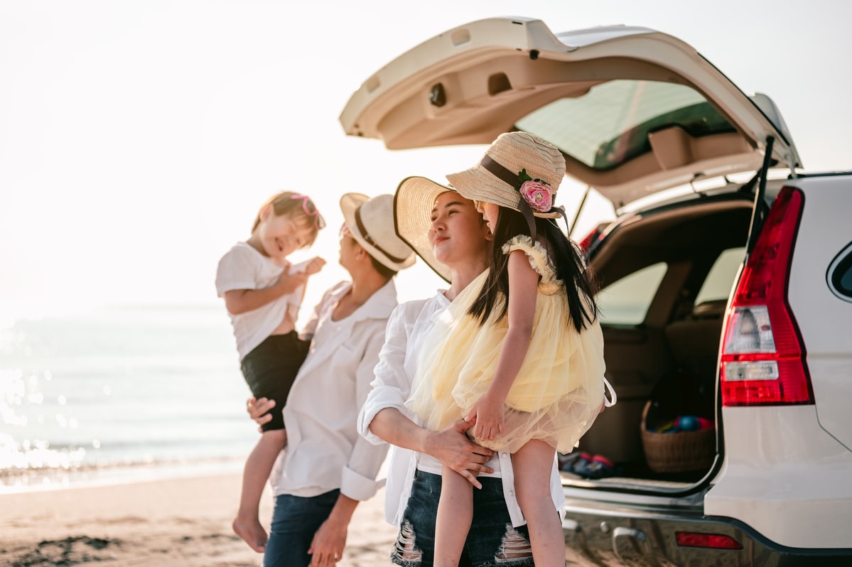 happy asian family on a road trip in their car. dad, mom and daughter are traveling by the sea.parents holding their children.summer ride by automobile.
