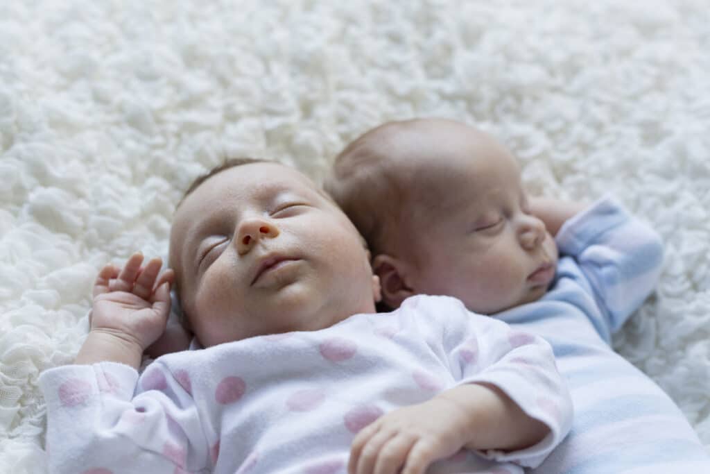 portrait of sleeping newborn baby girl lying besides her twin brother