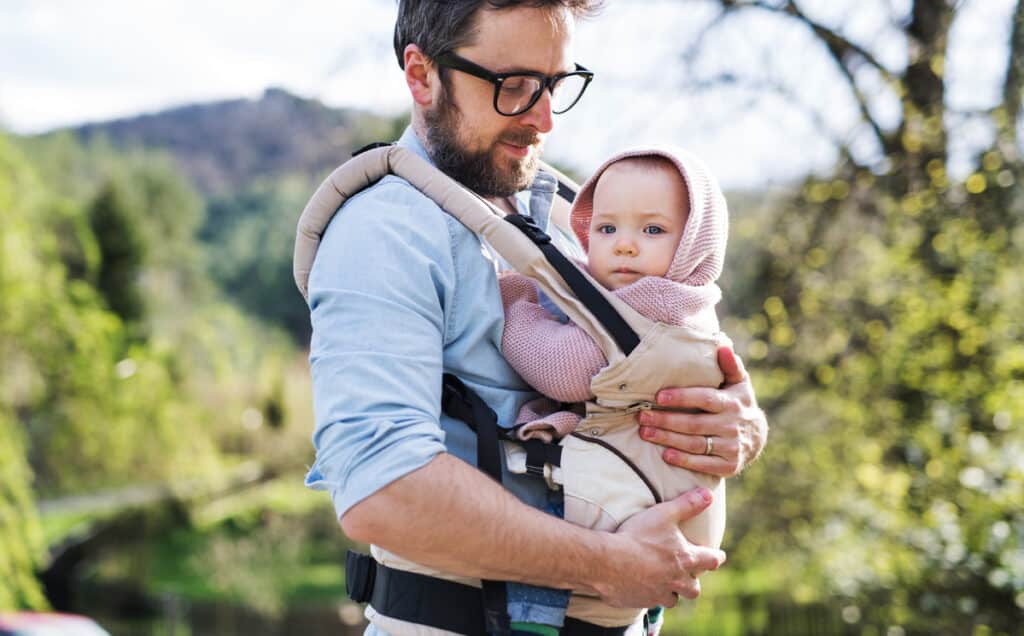 a father with his toddler daughter in a baby carrier outside on a spring walk.