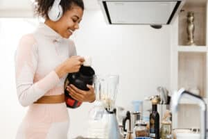 black woman in headphones making smoothie with protein at home