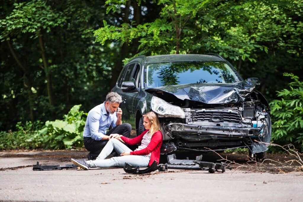 young woman by the car after an accident and a man making a phone call.